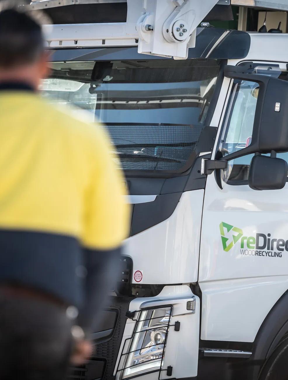 Hi-vis worker standing in front of reDirect Wood Recycling truck cab.