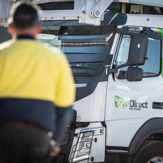 Hi-vis worker standing in front of reDirect Wood Recycling truck cab.