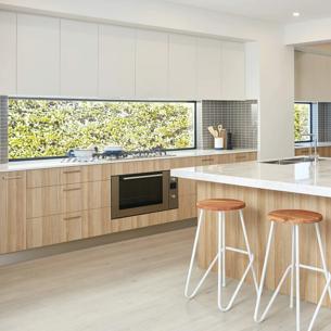A spacious kitchen with light wooden cabinets, white countertops, a steel refrigerator, stainless steel appliances, and modern furniture