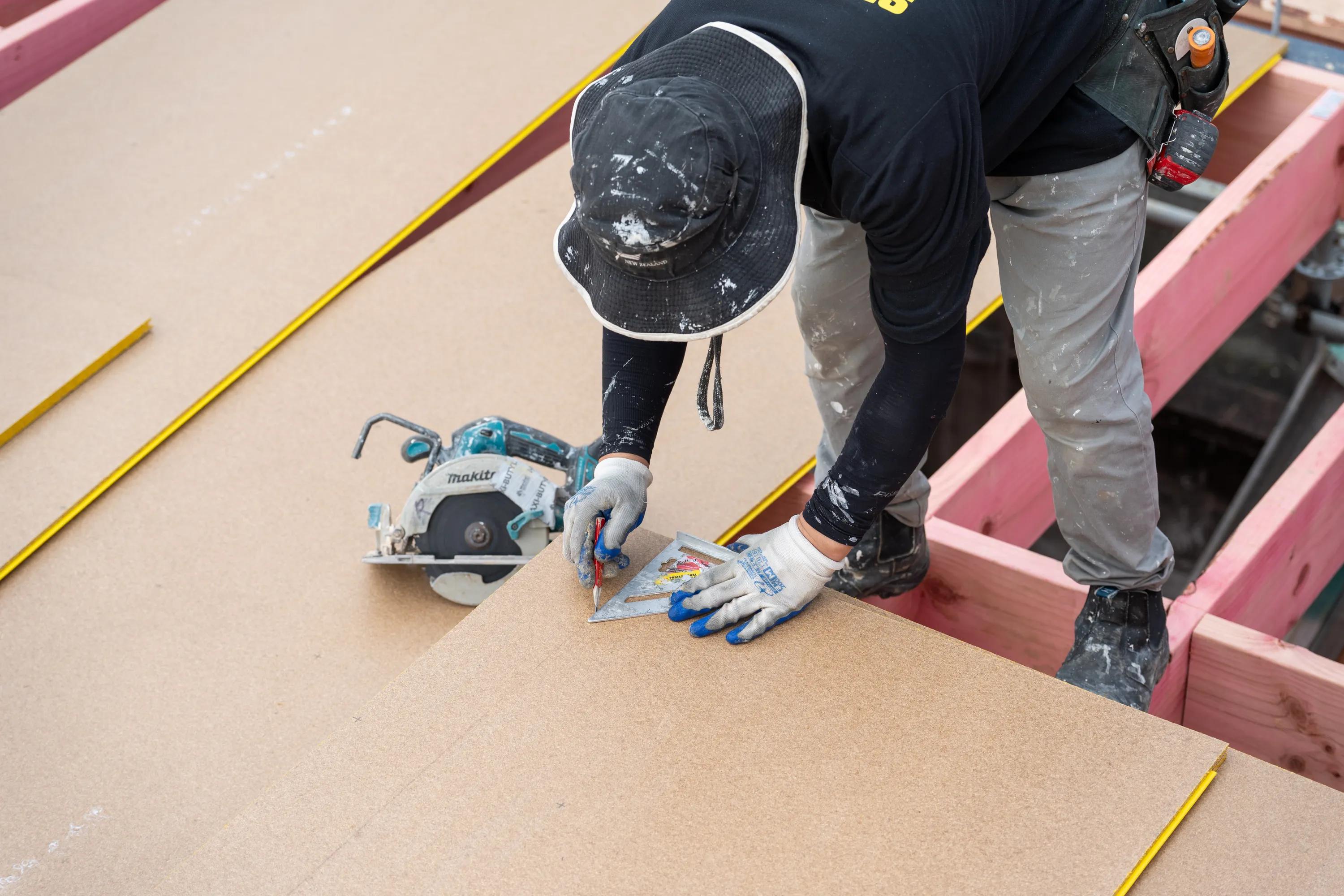 Worker measuring and cutting a sheet panel with a circular saw on a timber-framed construction site