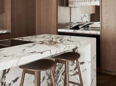A well-lit kitchen interior featuring a modern design, marble countertops, wood cabinets, a wine glass rack, and stainless steel appliances