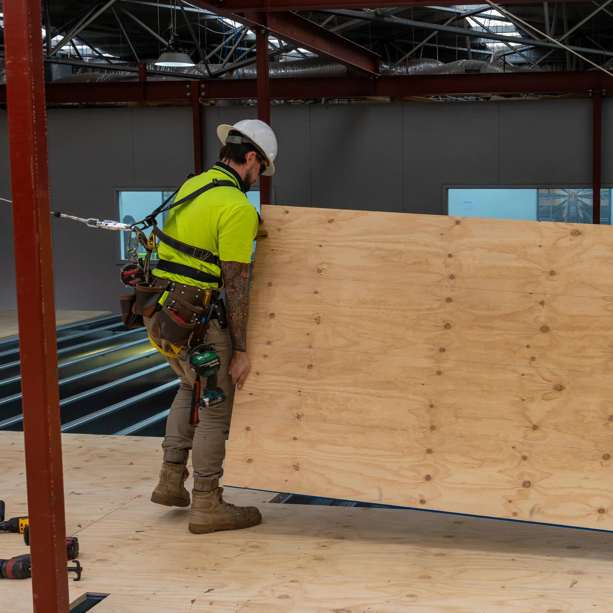 Workers installing STRUCTAply plywood flooring panels inside a steel-framed building