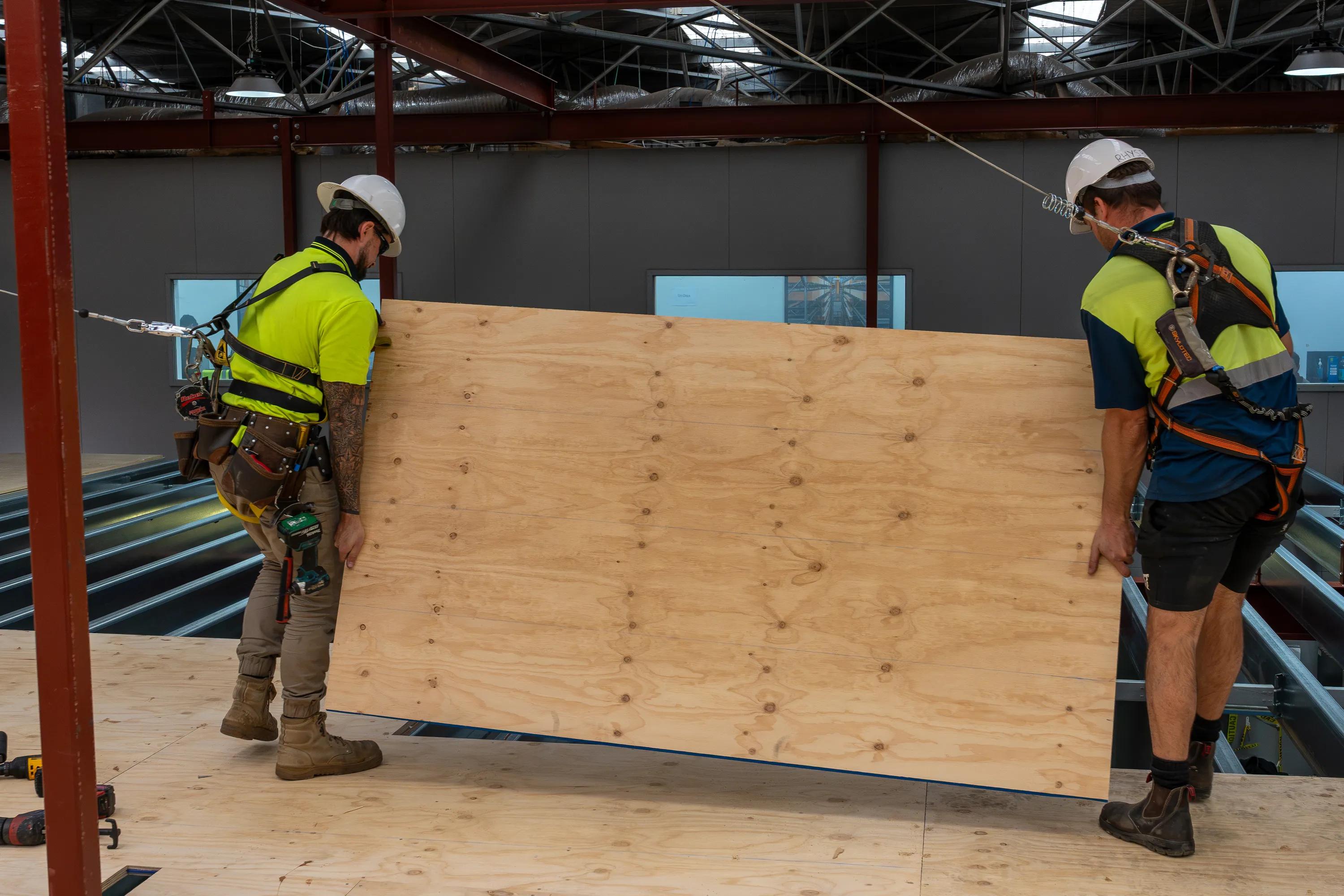Workers installing STRUCTAply plywood flooring panels inside a steel-framed building