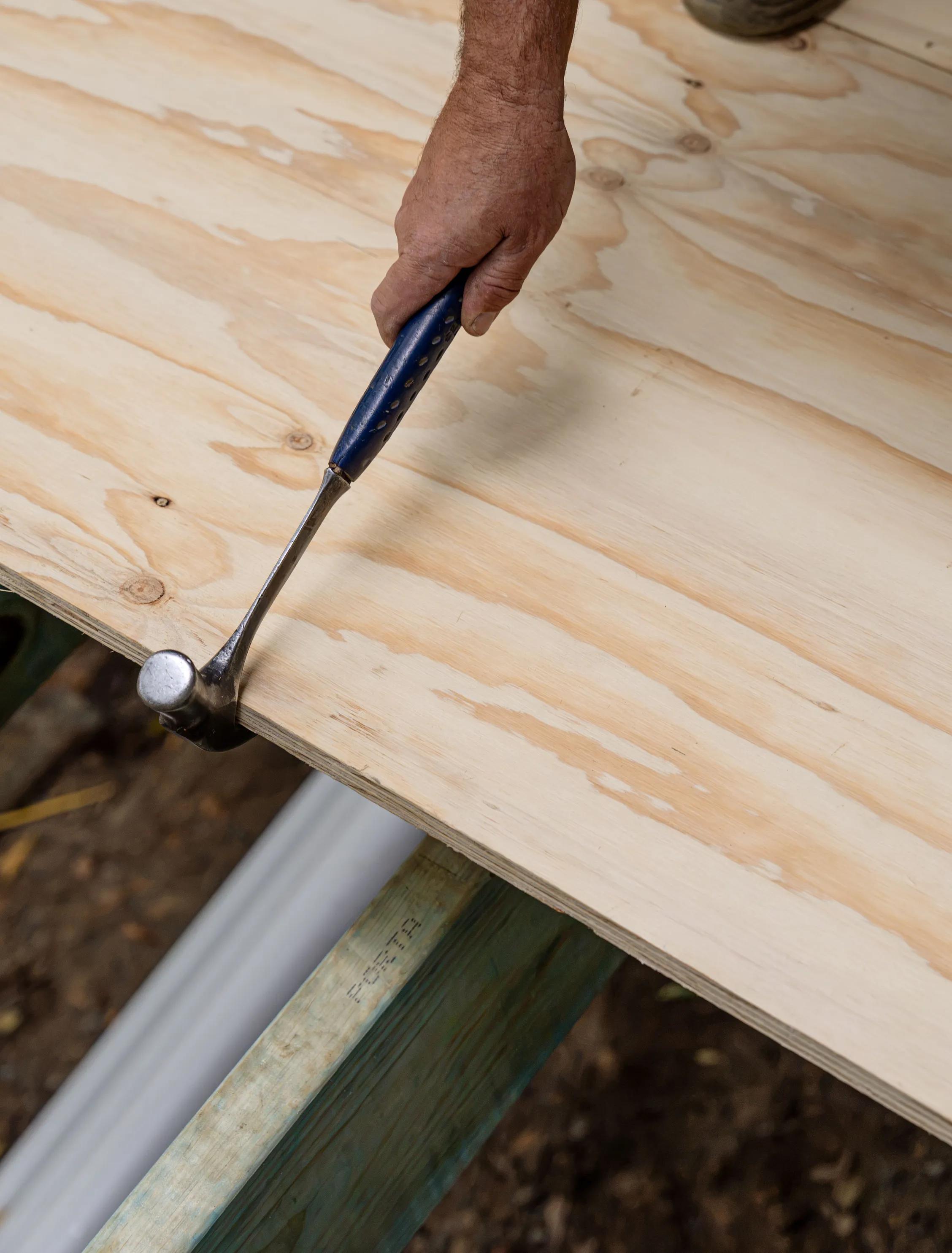 Hand using a screwdriver to tighten a fastener on the edge of a wooden board.