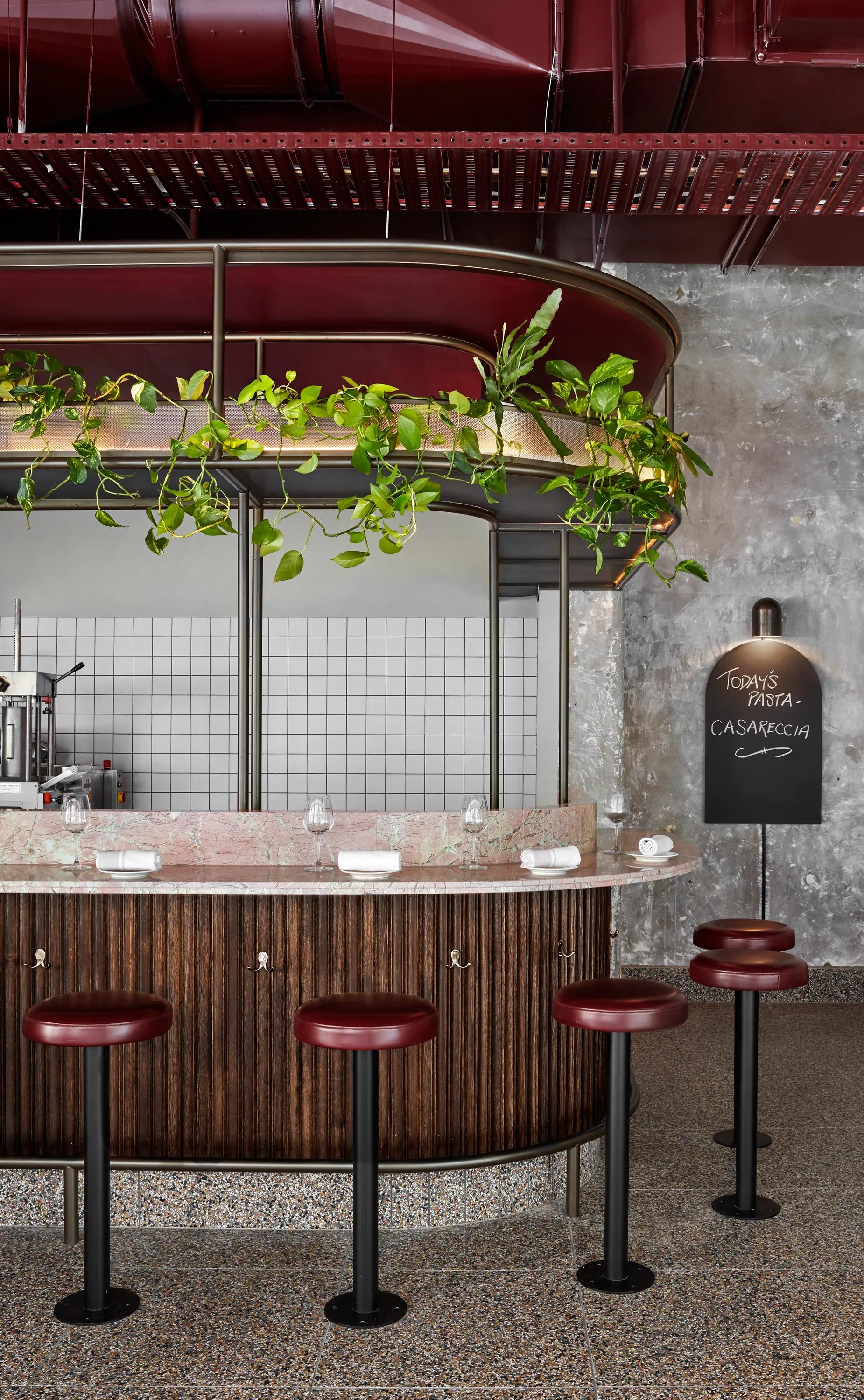 Restaurant interior with red stools, a wooden bar, hanging lights, and wall shelving
