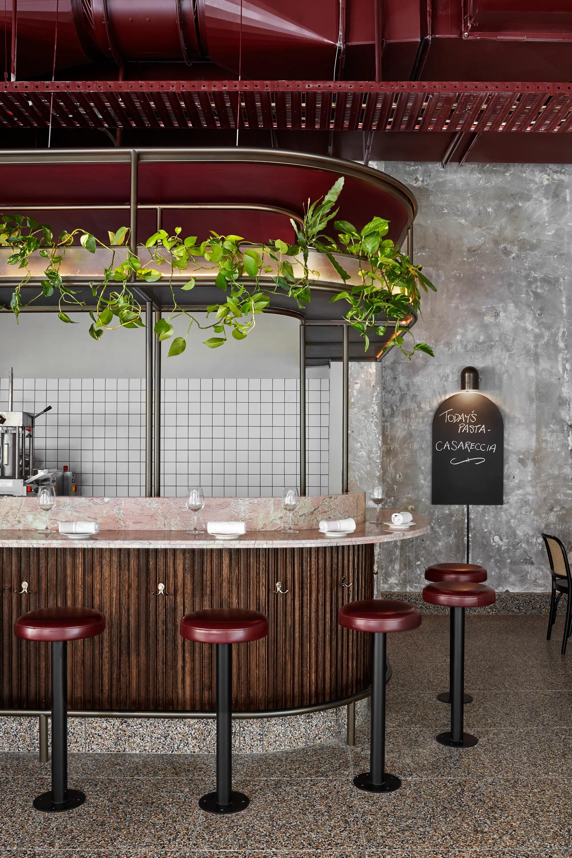 Restaurant interior with red stools, a wooden bar, hanging lights, and wall shelving