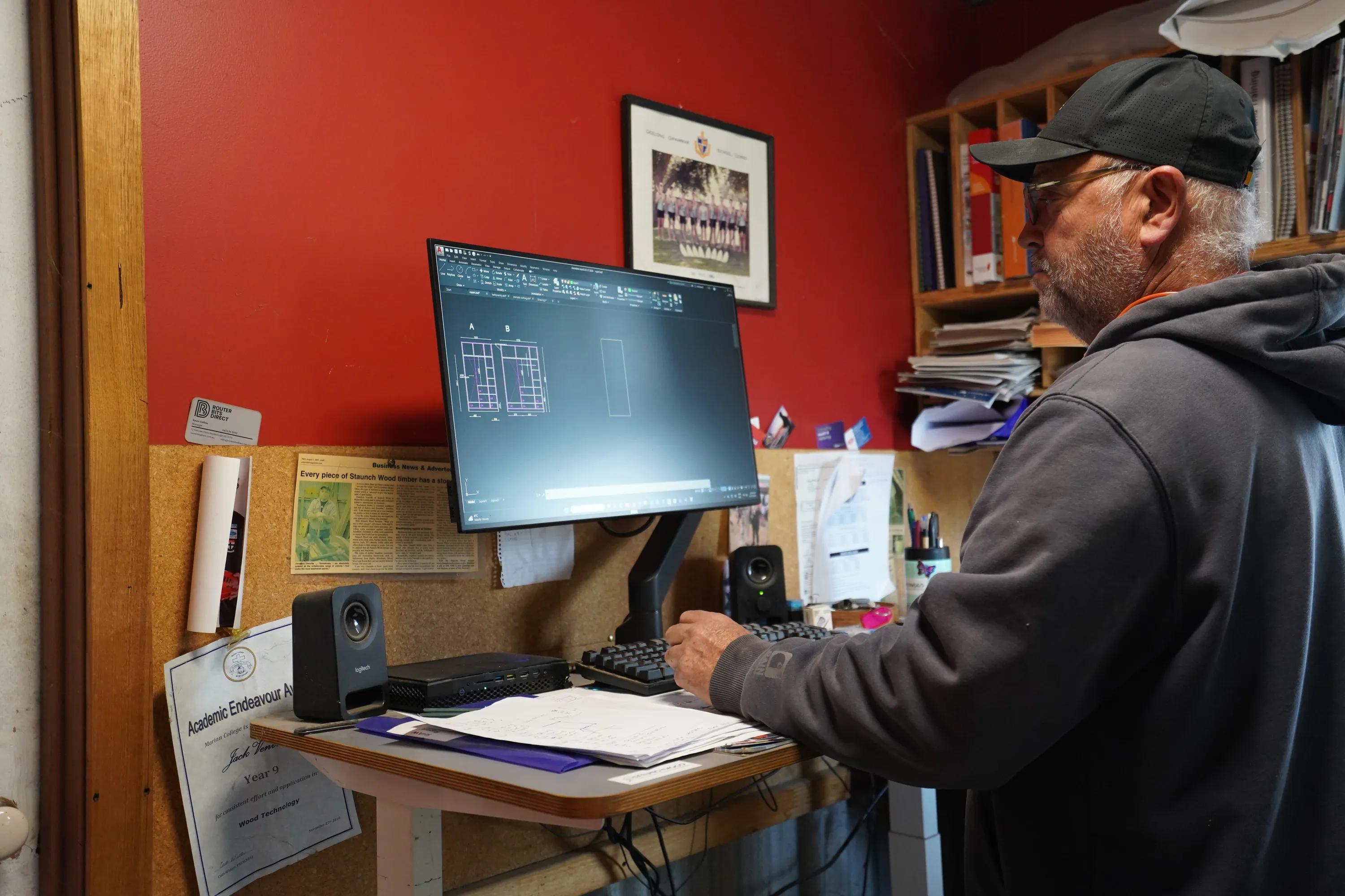 Person using CAD software at a desk in a home office, with STRUCTAply materials visible nearby