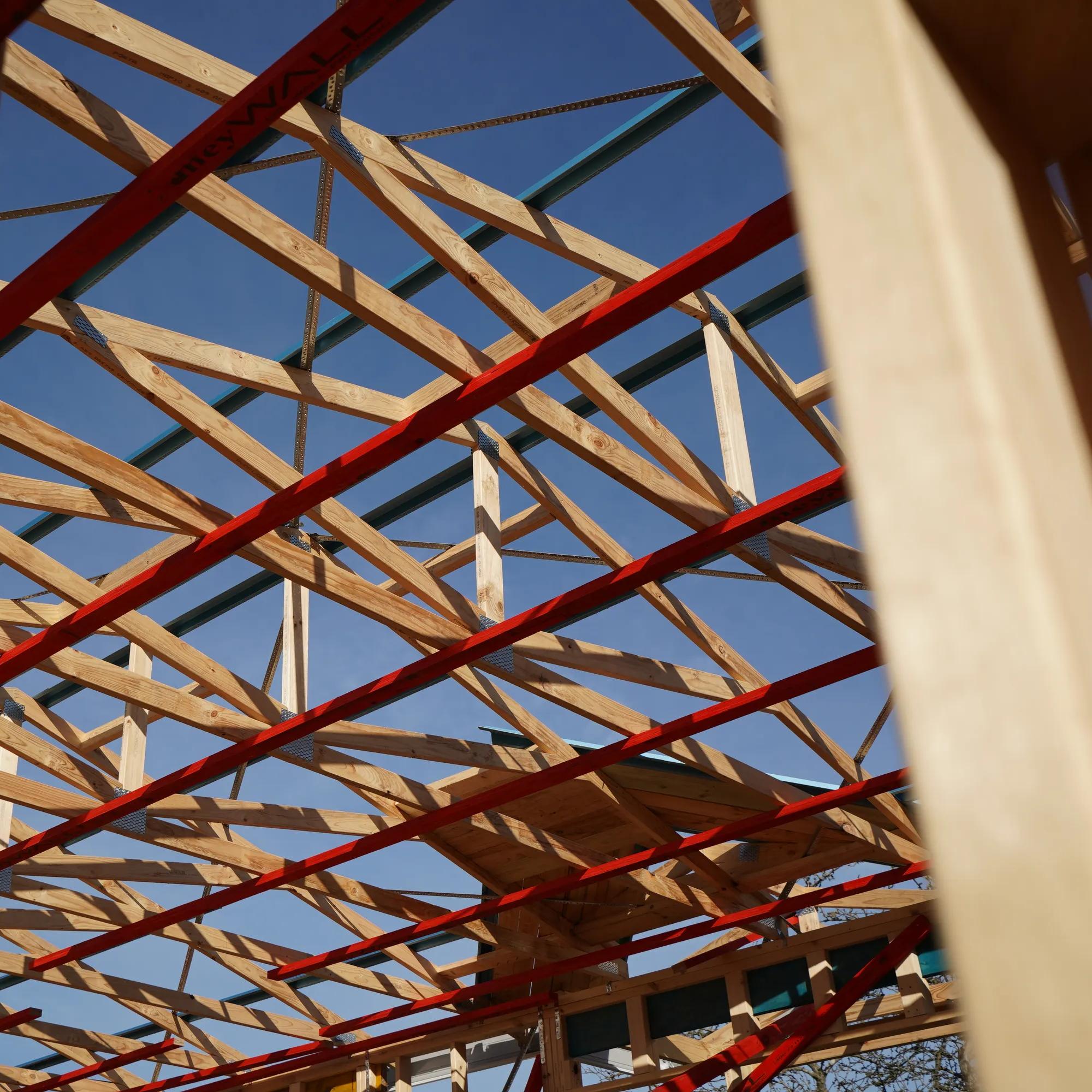 Porta timber roof framing with exposed trusses and red structural supports against a blue sky