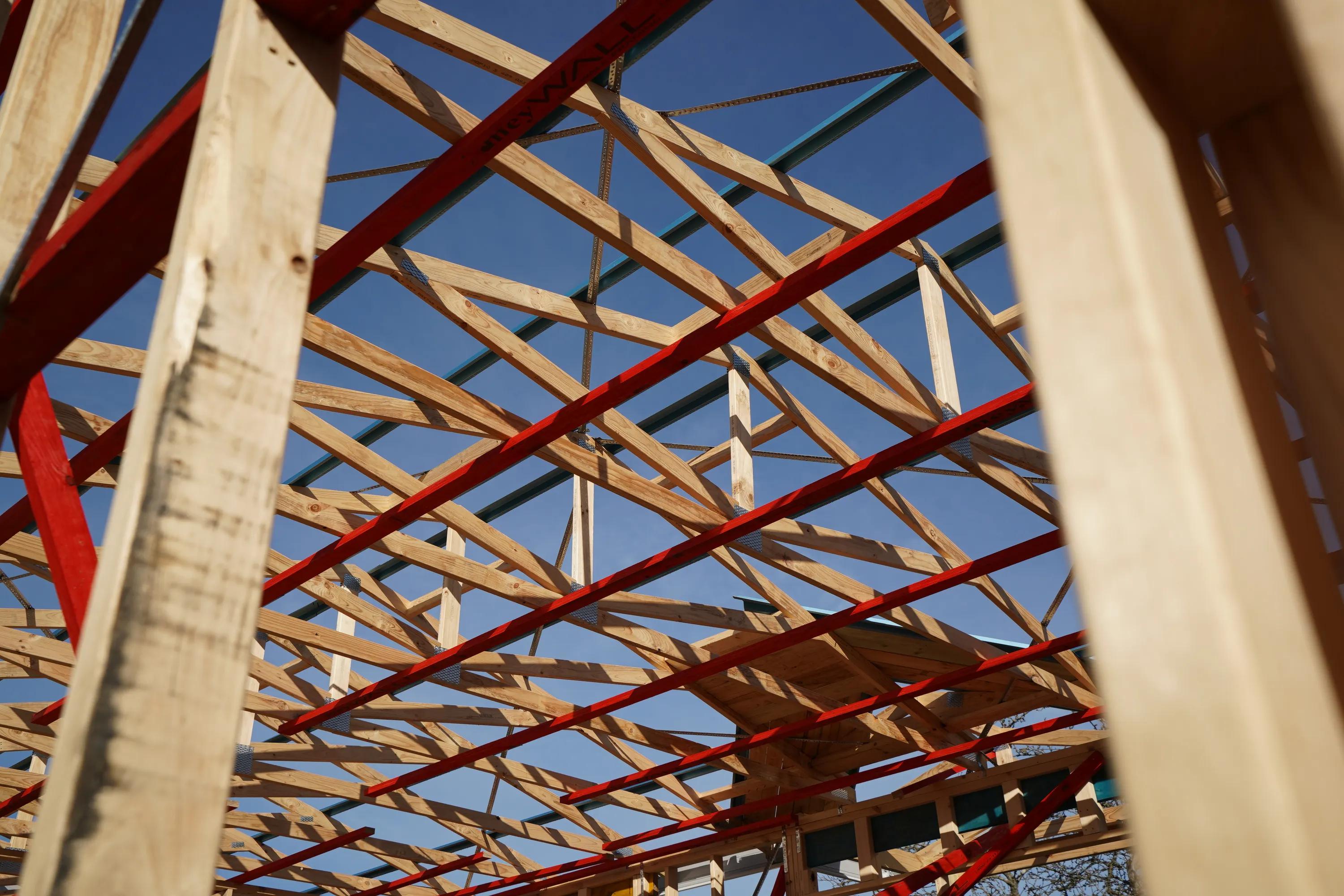 Porta timber roof framing with exposed trusses and red structural supports against a blue sky
