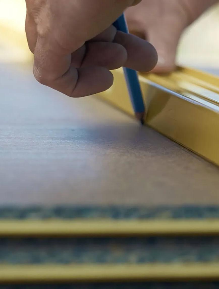 Person holding a measuring tape next to piece of wood