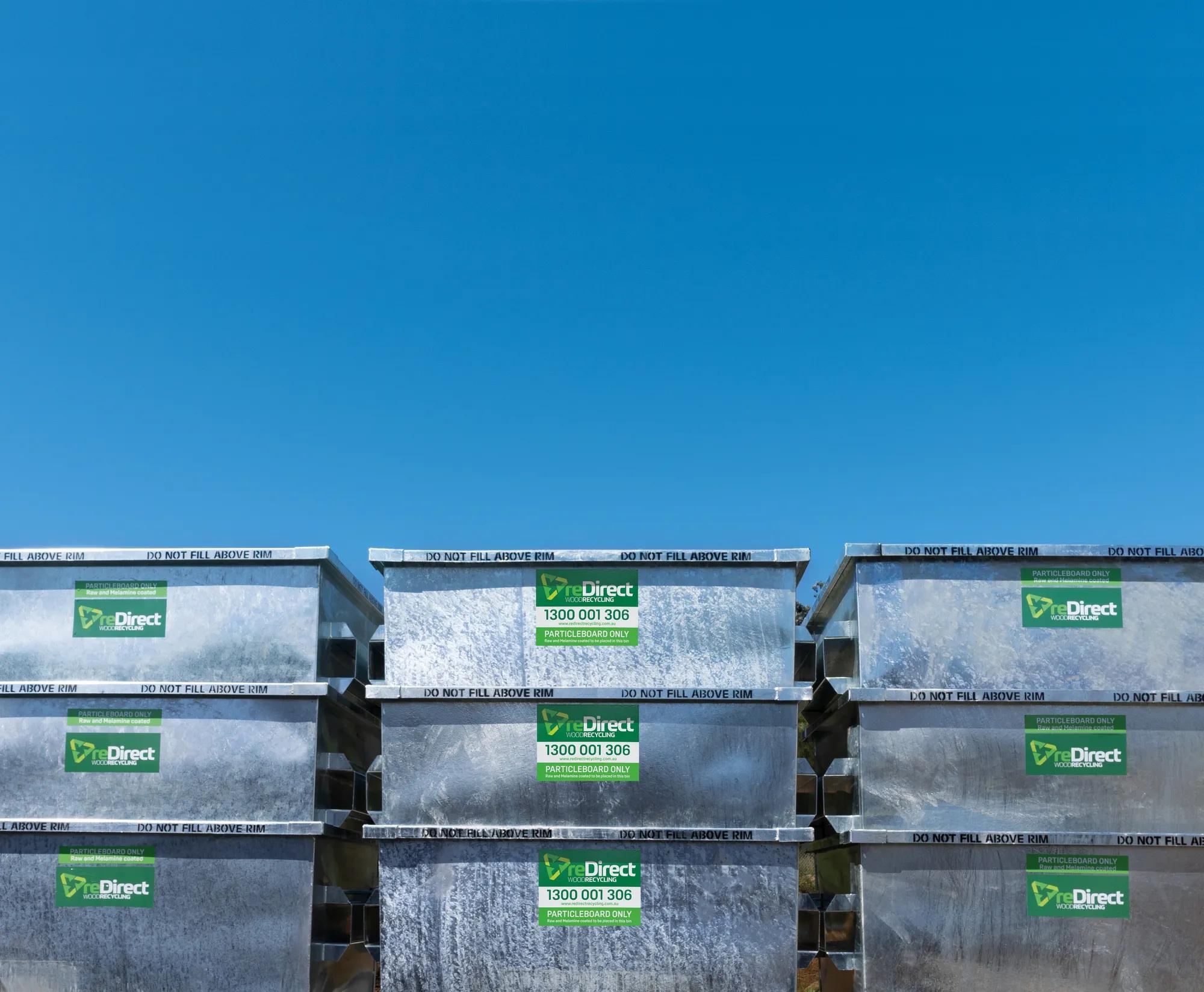 reDirect particleboard-only skip bins stacked outdoors against blue sky.