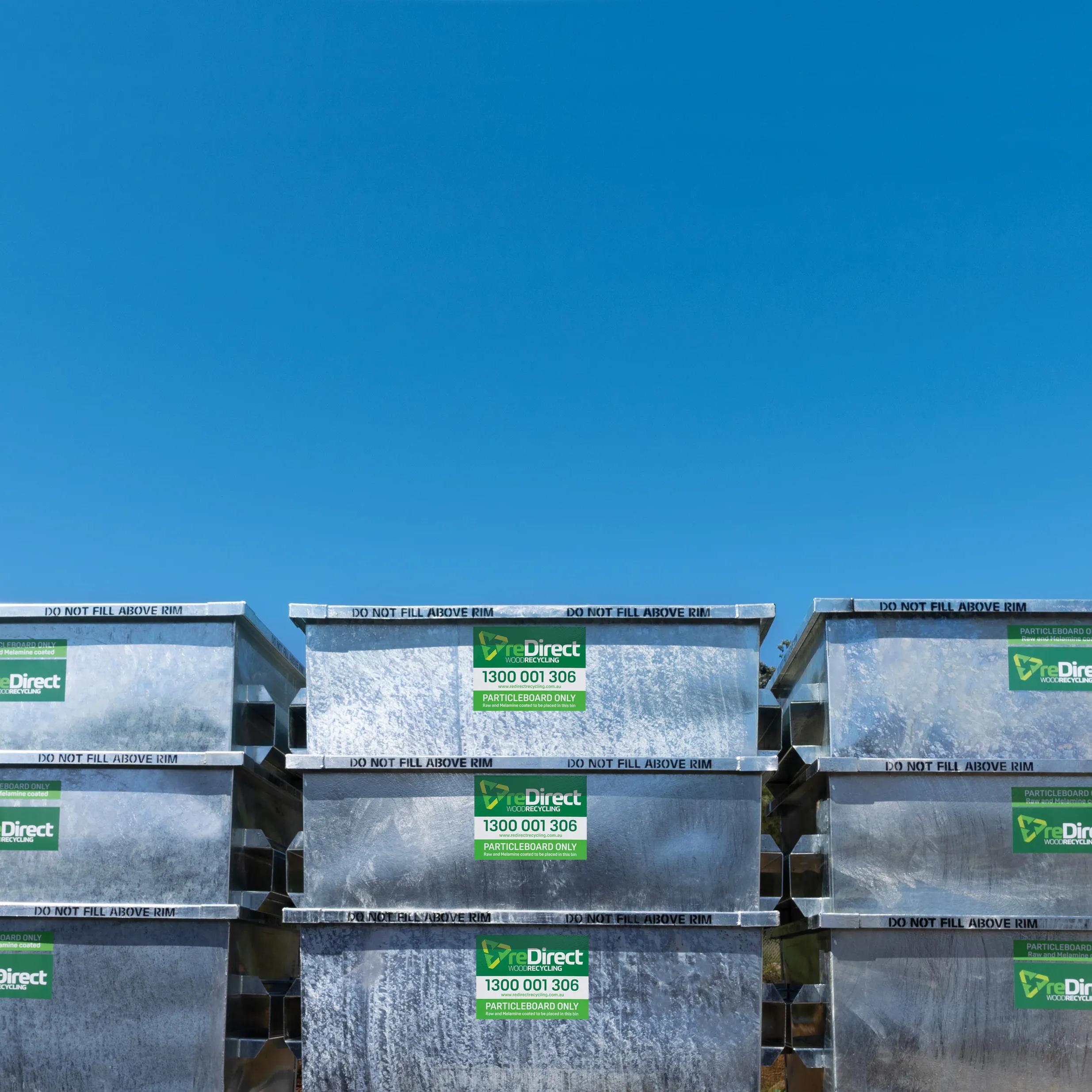 reDirect particleboard-only skip bins stacked outdoors against blue sky.