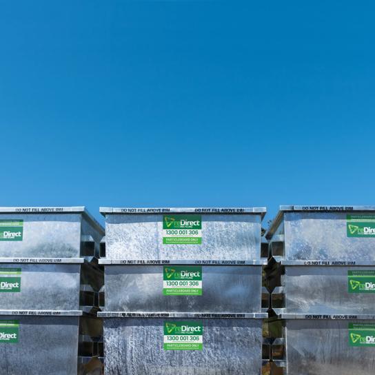 reDirect particleboard-only skip bins stacked outdoors against blue sky.