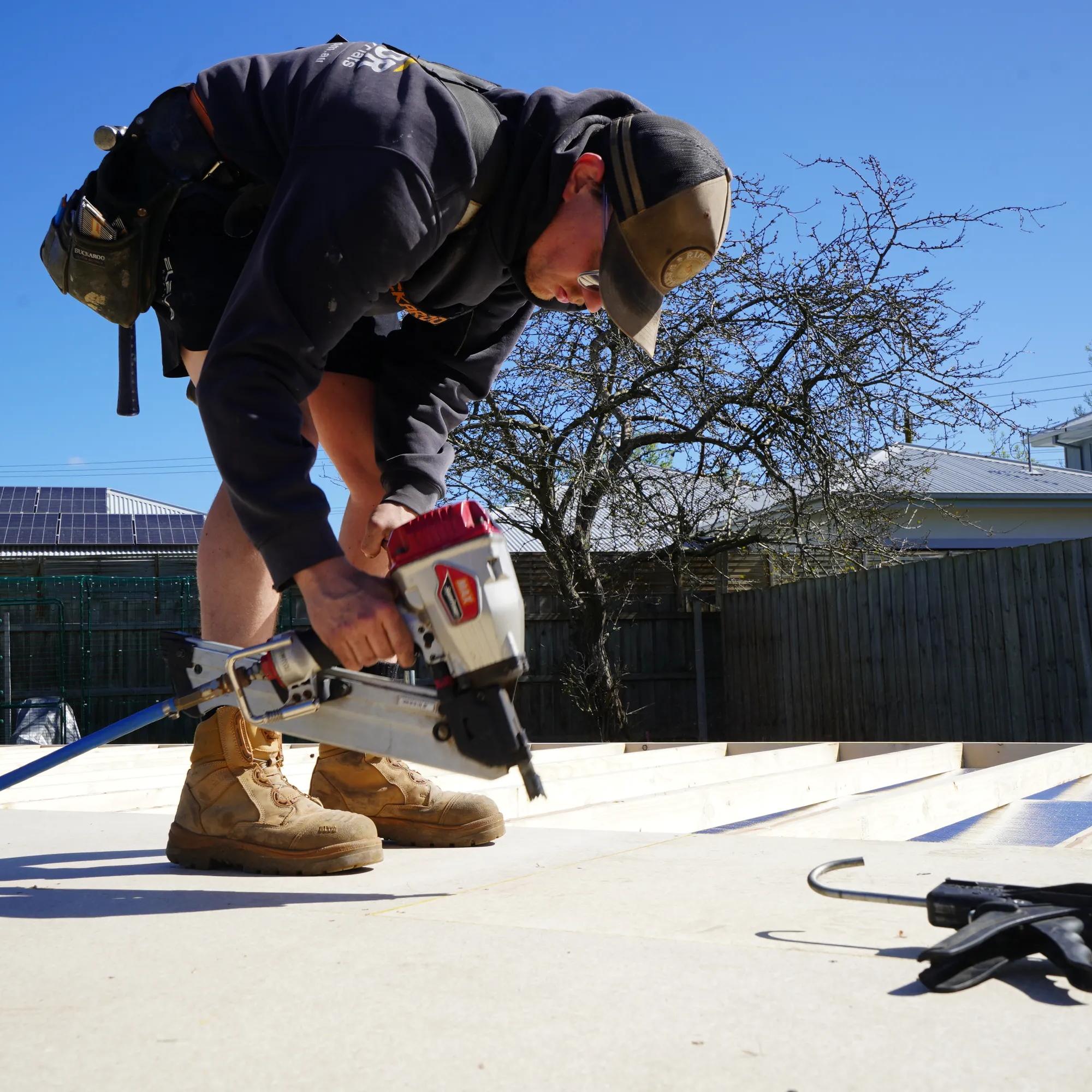 Worker using a pneumatic nail gun while installing roofing panels on a residential roof
