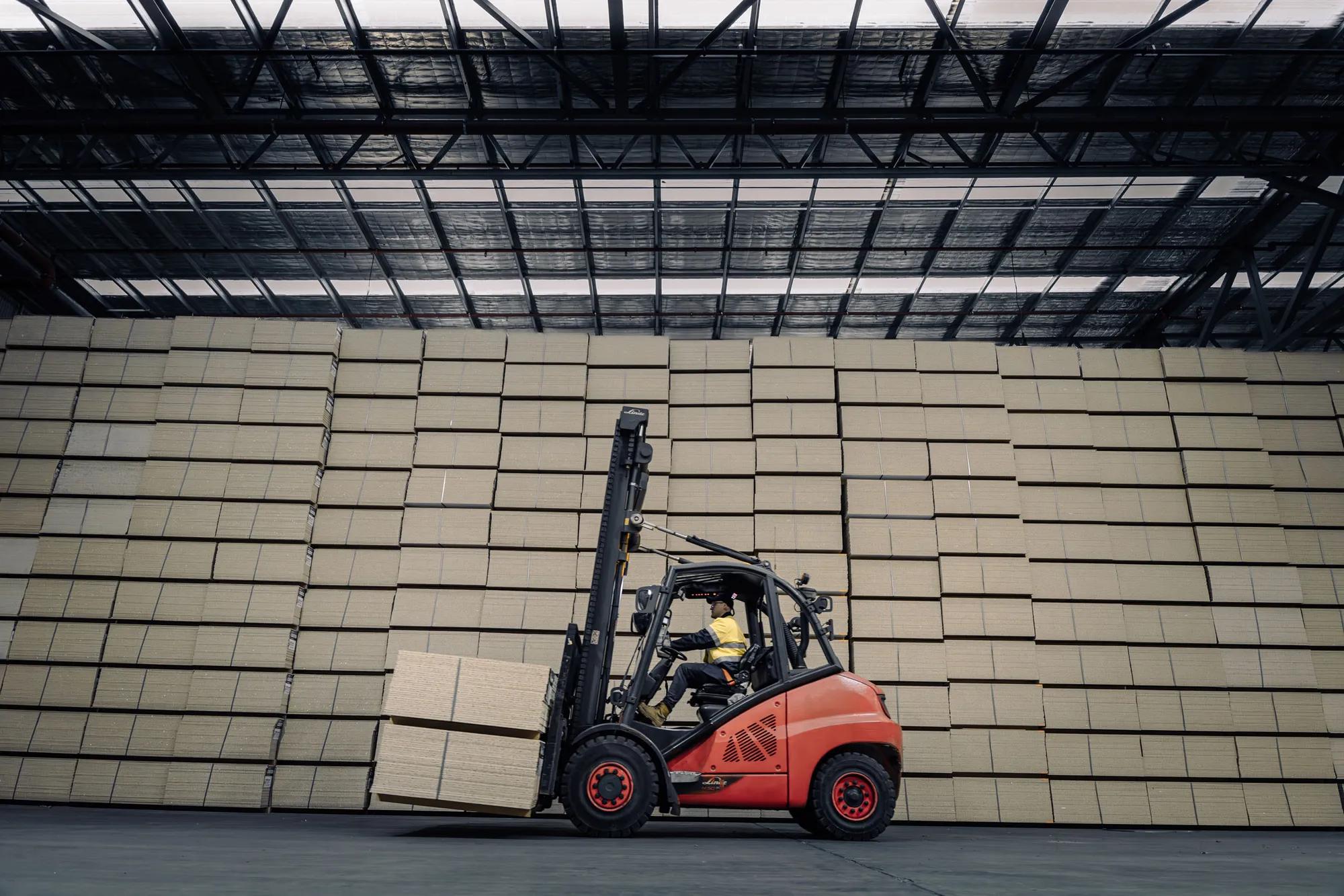 Large stack of STRUCTAflor panels inside a warehouse with a forklift carrying more panels
