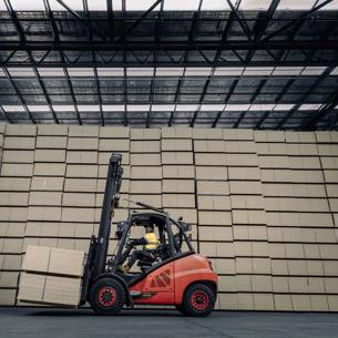 Large stack of STRUCTAflor panels inside a warehouse with a forklift carrying more panels