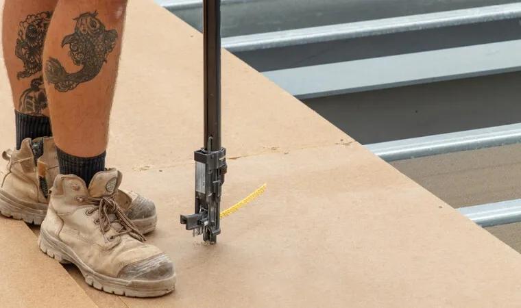 Two photos of a person wearing boots, pants, and a black shirt with visible tattoos, standing on what appears to be construction material
