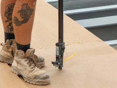 Two photos of a person wearing boots, pants, and a black shirt with visible tattoos, standing on what appears to be construction material