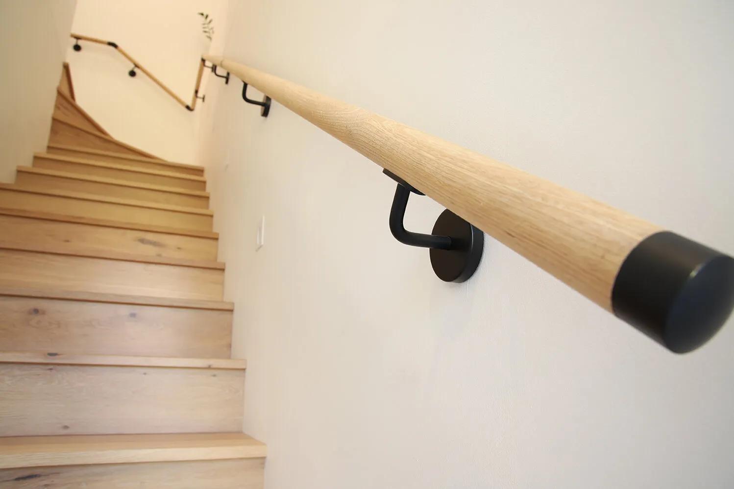 A wooden handrail is attached to a wall next to a staircase