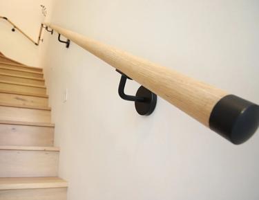 A wooden handrail is attached to a wall next to a staircase