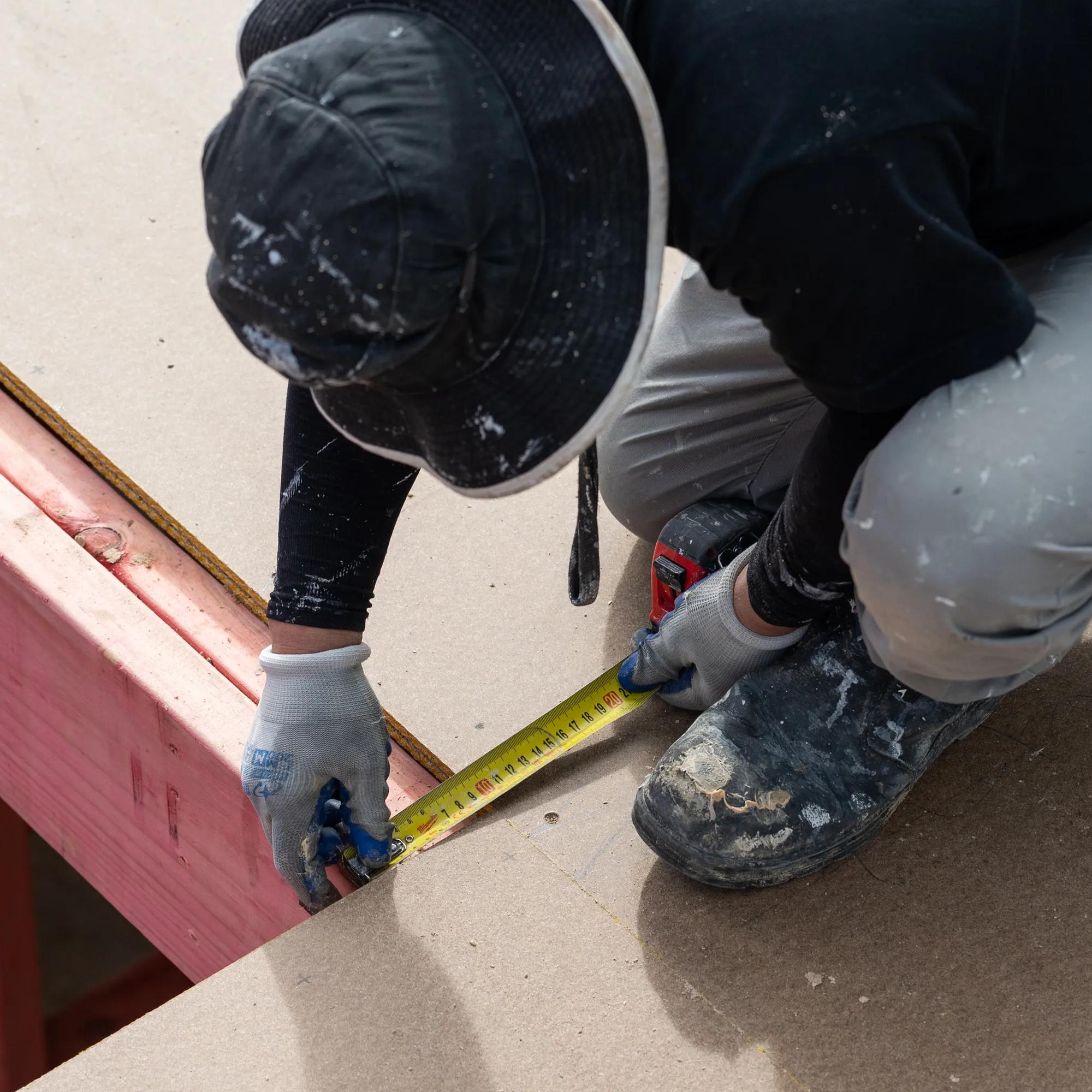 Worker measuring a pink timber frame with a tape measure during construction