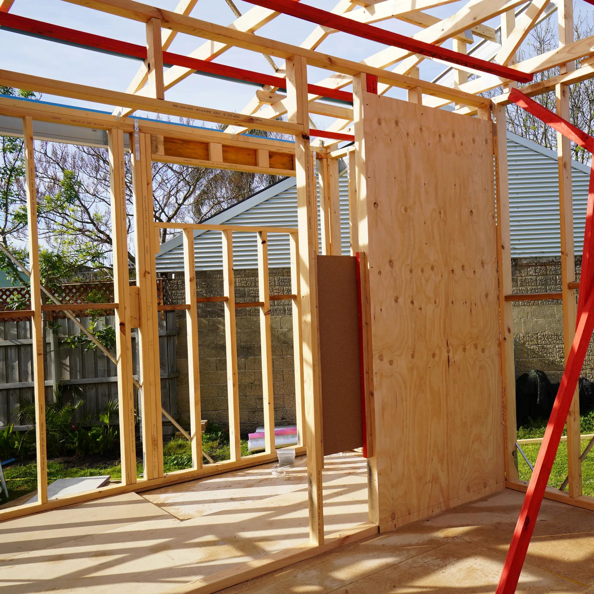 Timber-framed house extension under construction with plywood sheeting and red bracing straps