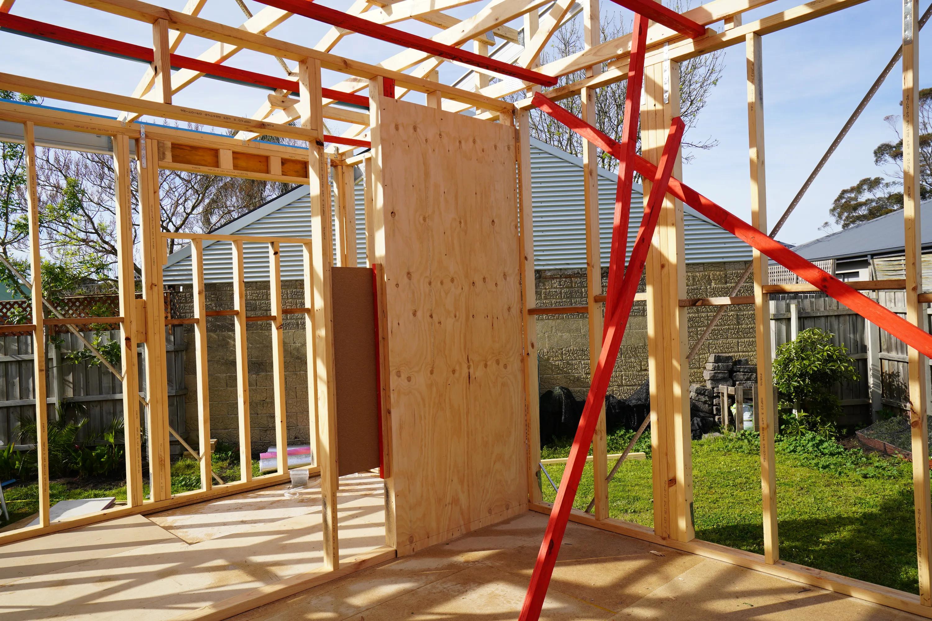 Timber-framed house extension under construction with plywood sheeting and red bracing straps