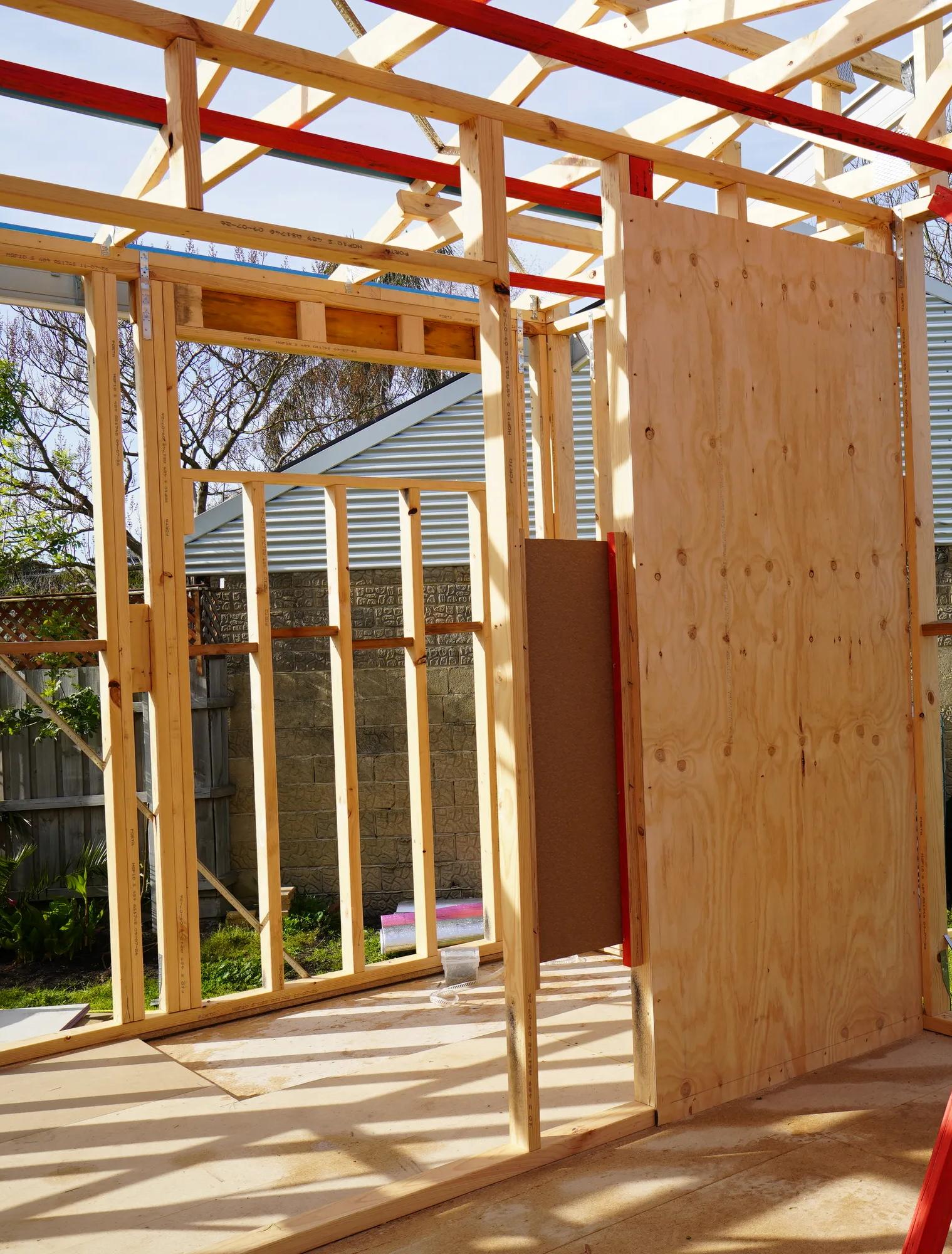 Timber-framed house extension under construction with plywood sheeting and red bracing straps