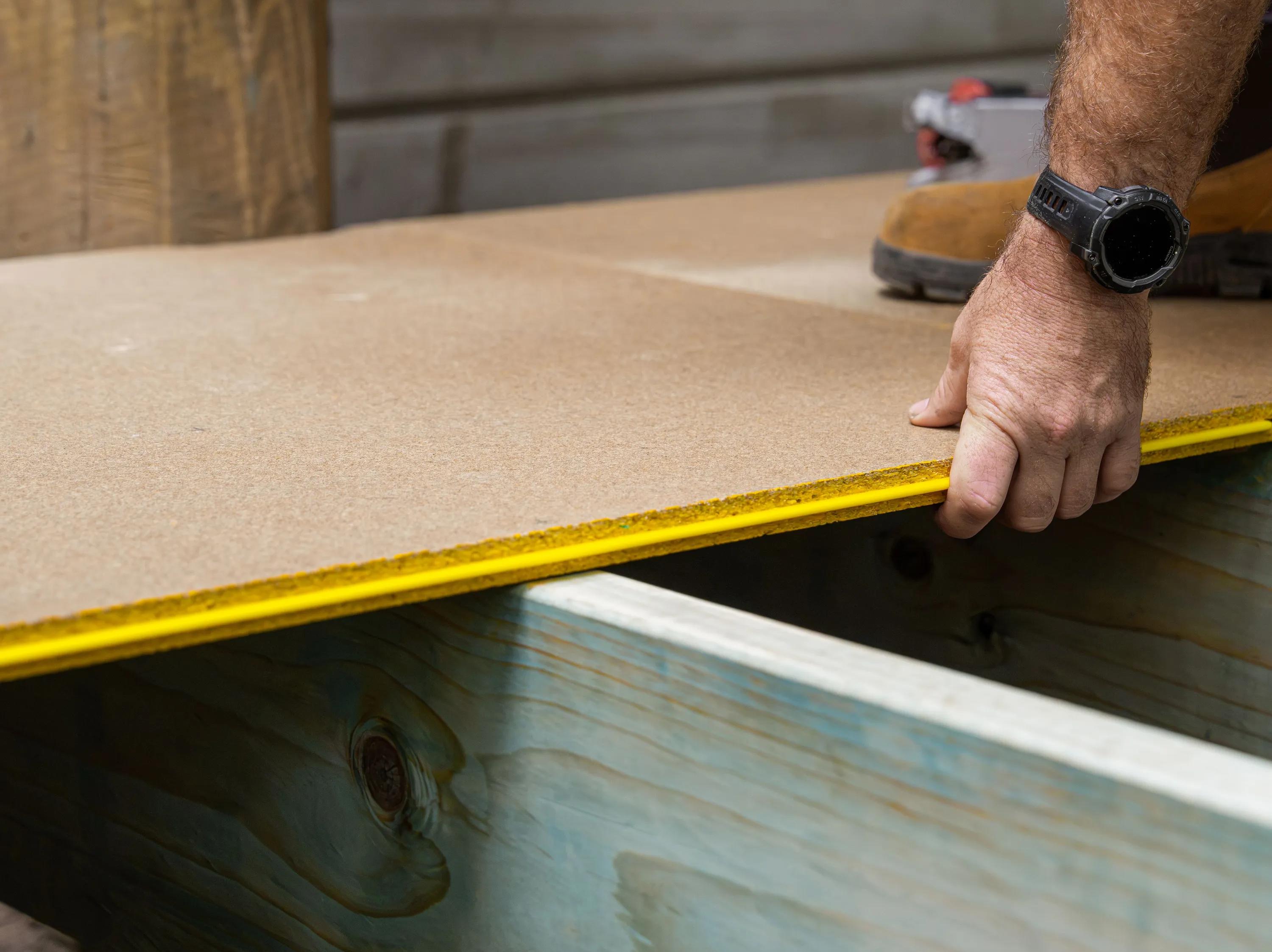 Person measuring a wood panel with a tape measure during construction