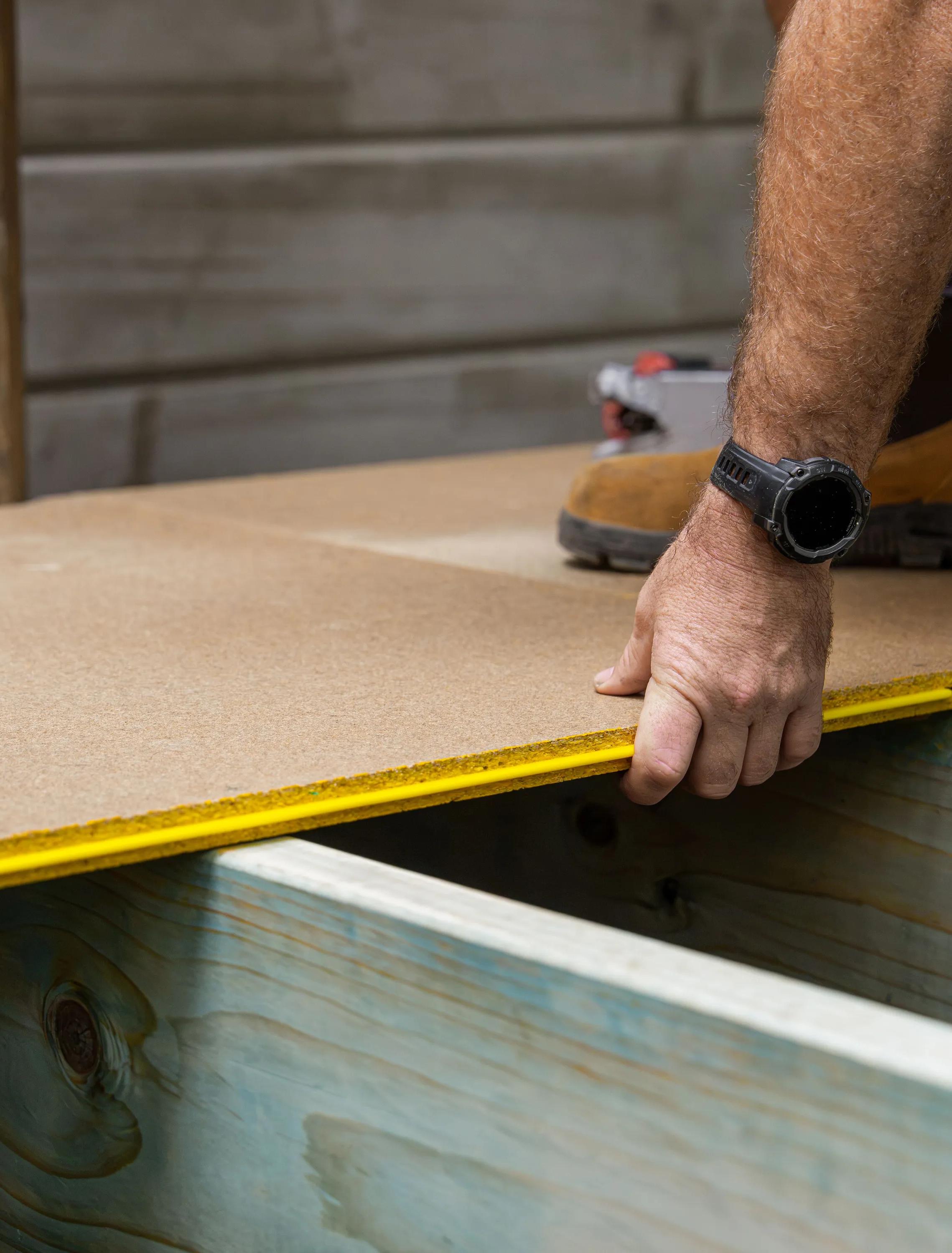Person measuring a wood panel with a tape measure during construction