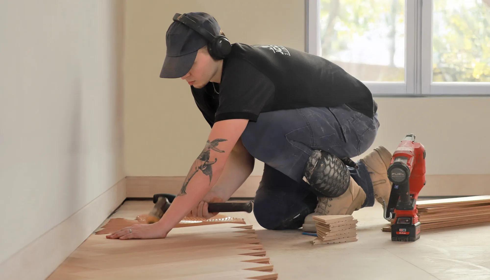 A man installing molding around a room. He's kneeling down to work on the wall
