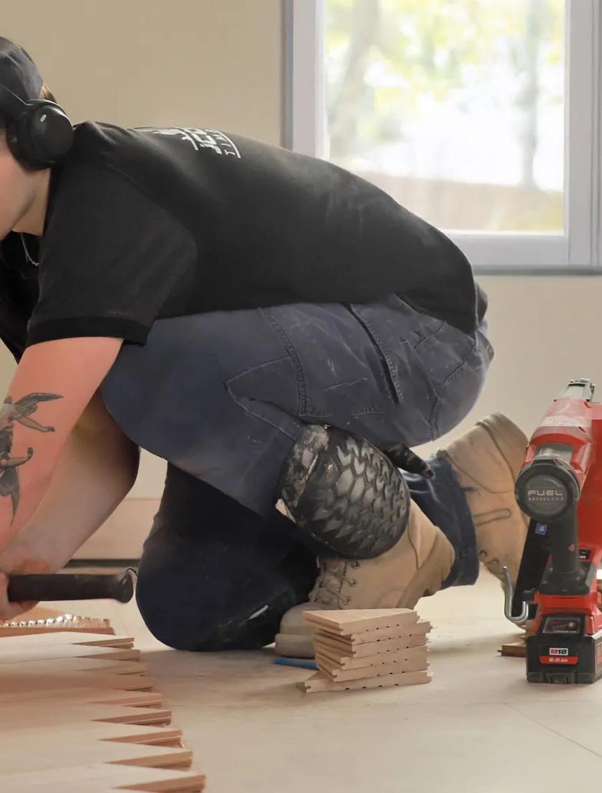 A man installing molding around a room. He's kneeling down to work on the wall