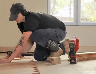 A man installing molding around a room. He's kneeling down to work on the wall