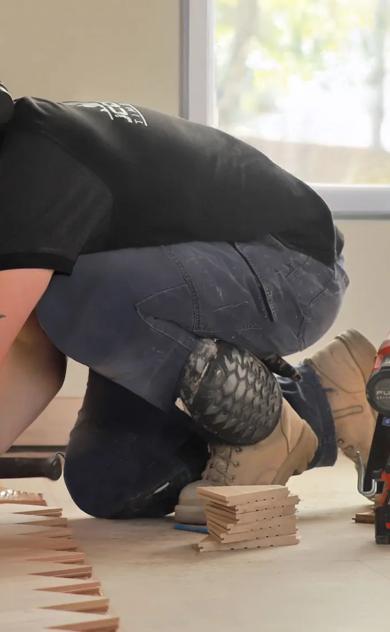 A man installing molding around a room. He's kneeling down to work on the wall