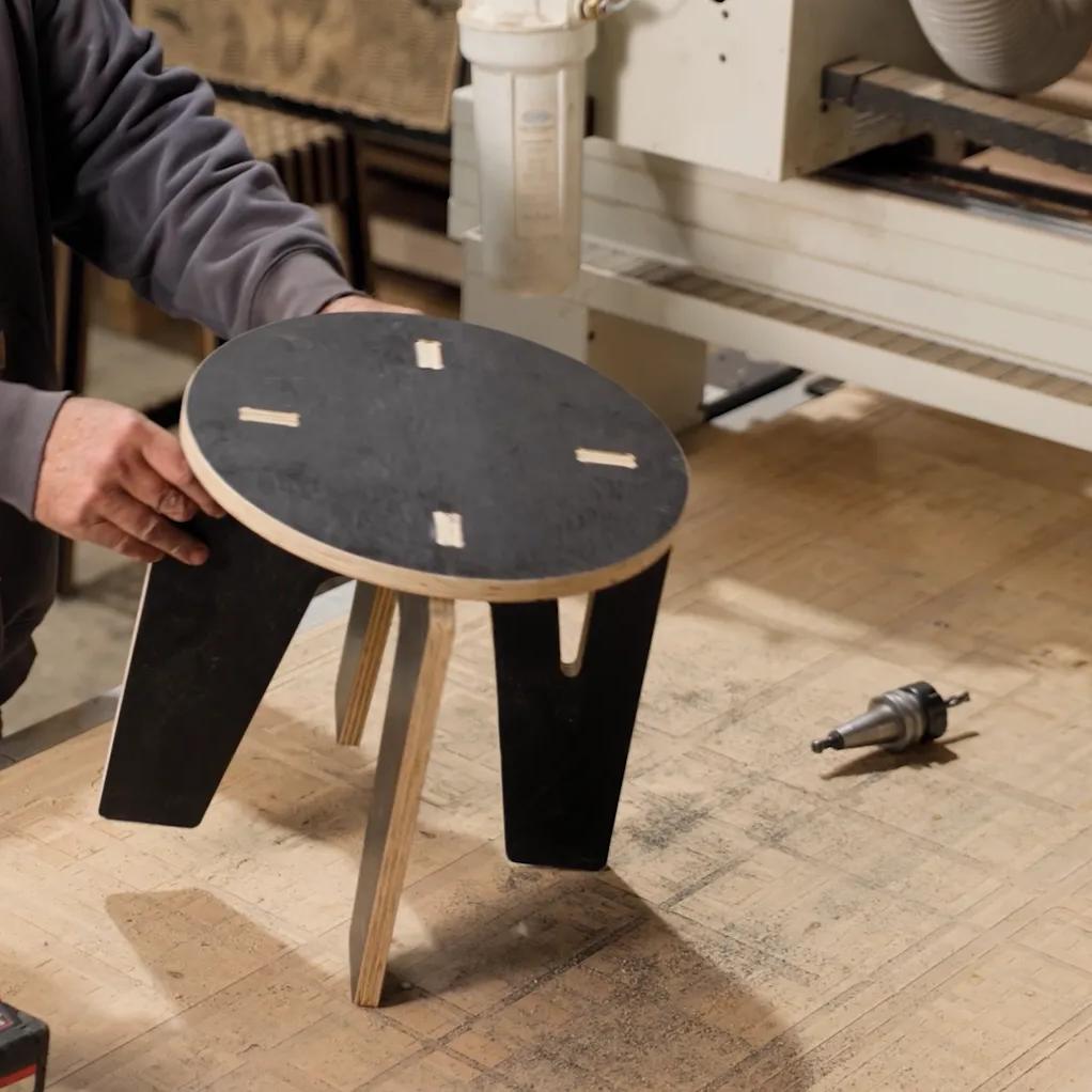 Person assembling a round black STRUCTAply stool in a workshop