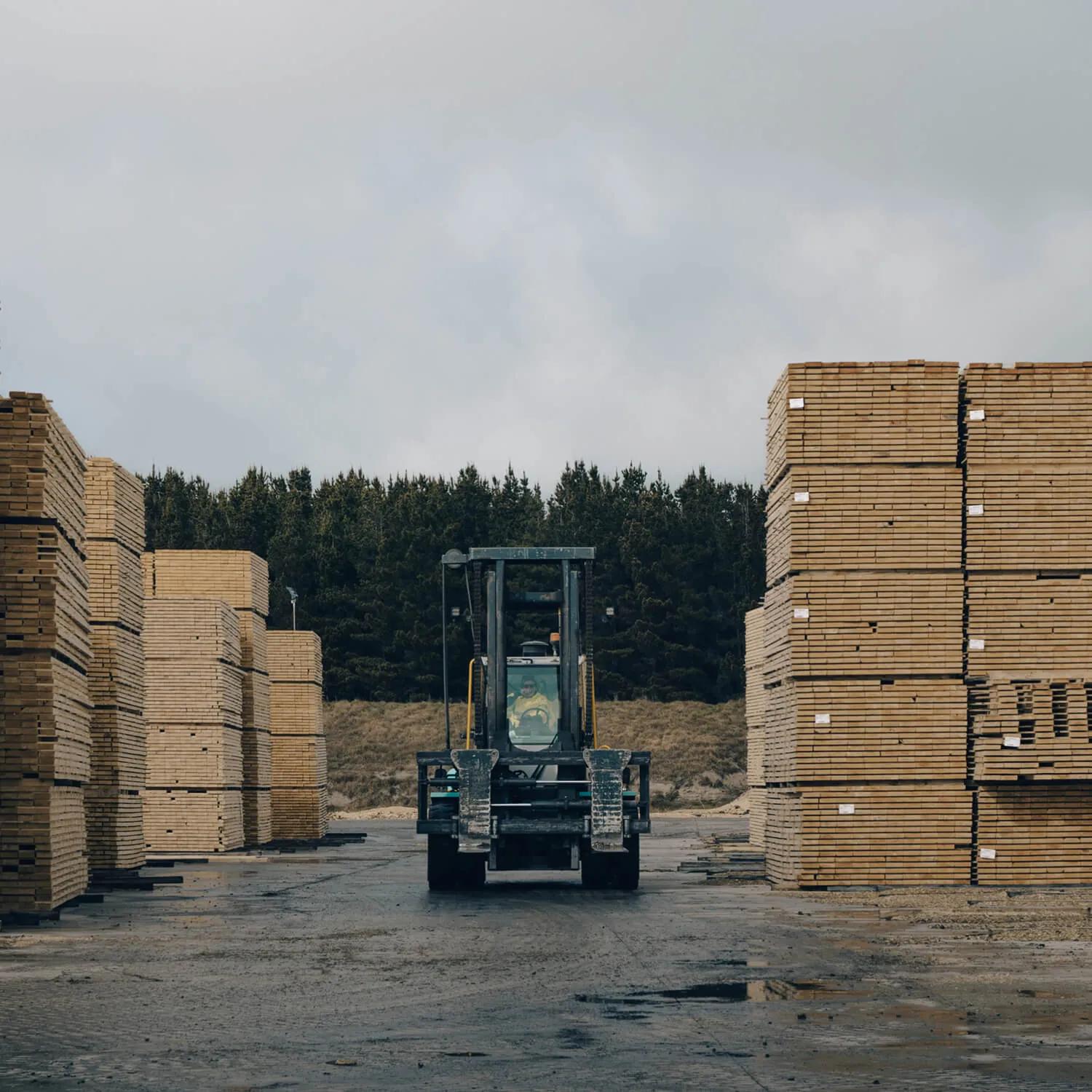 A truck driving between two tall stacks of timber on a flat surface