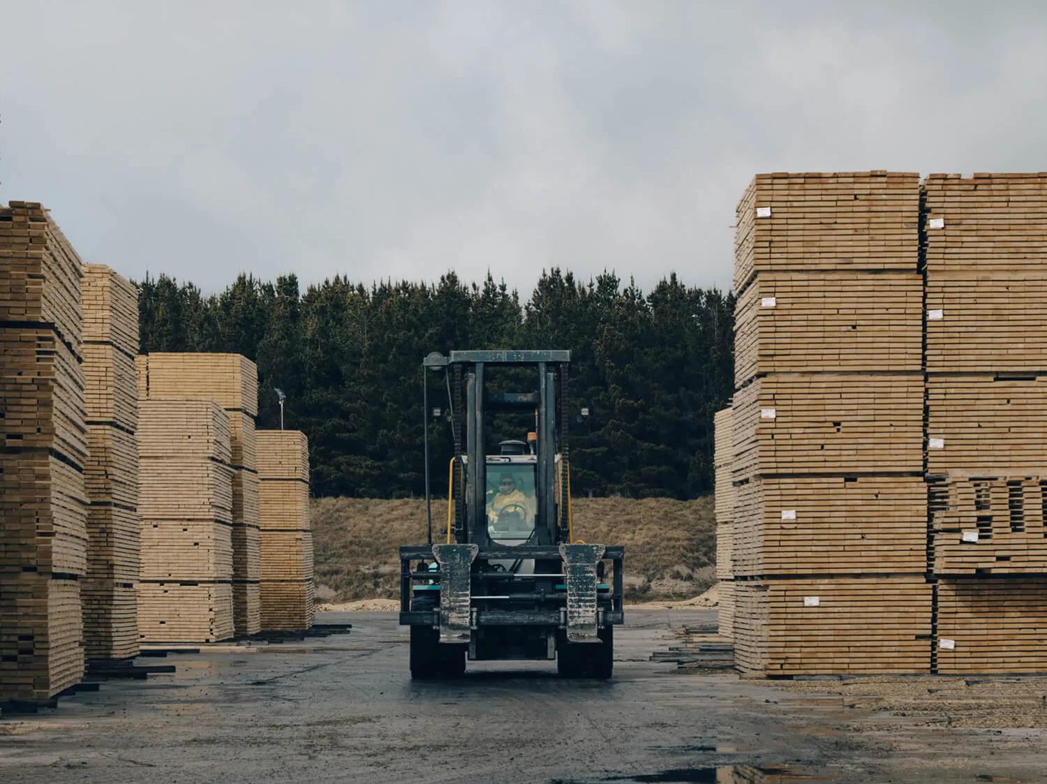 A truck driving between two tall stacks of timber on a flat surface