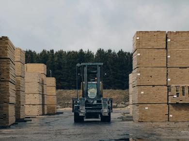 A truck driving between two tall stacks of timber on a flat surface