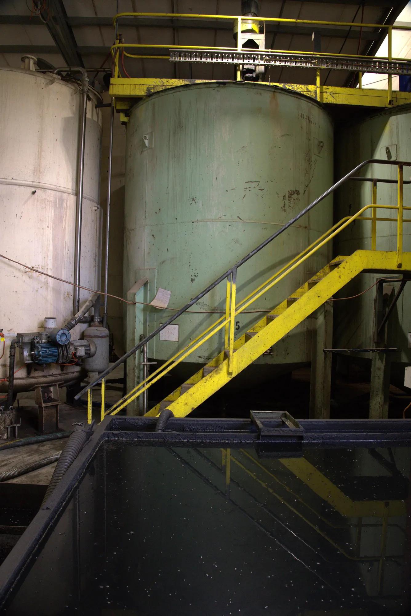 Large industrial liquid storage tank with yellow safety staircase inside facility.
