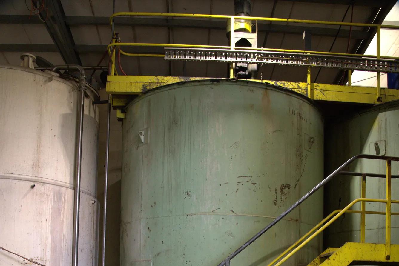 Large industrial liquid storage tank with yellow safety staircase inside facility.