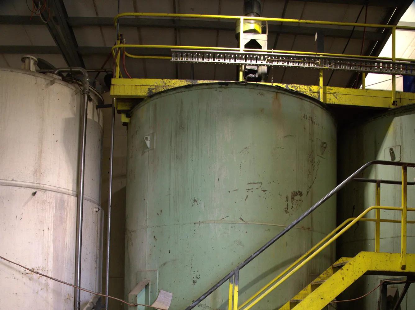 Large industrial liquid storage tank with yellow safety staircase inside facility.