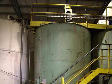 Large industrial liquid storage tank with yellow safety staircase inside facility.
