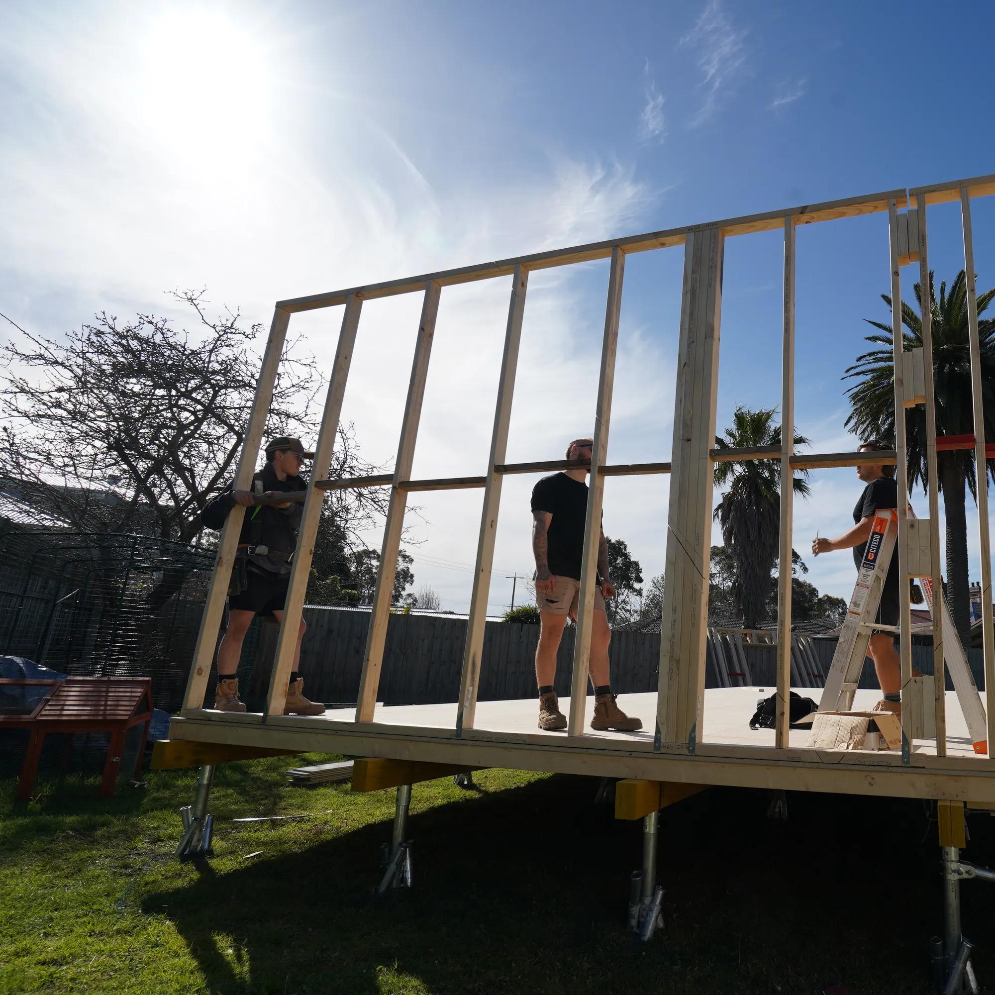 Timber wall framing being installed on a raised house platform outdoors