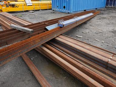 Rusty steel beams and scrap metal at recycling yard with shipping containers.