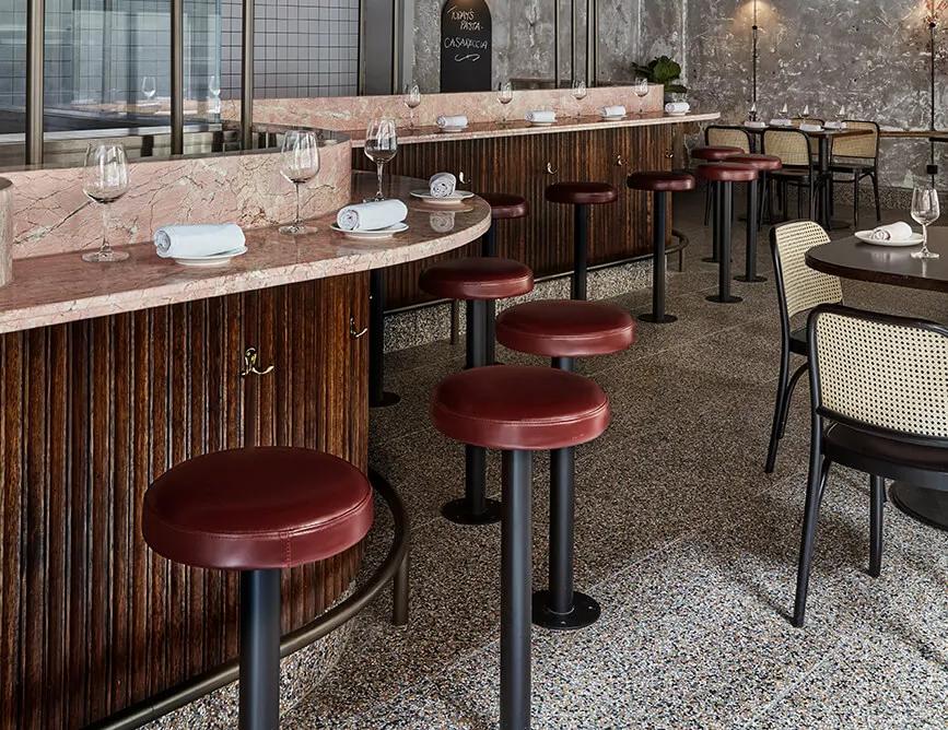 A modern restaurant interior with a contemporary design featuring plants, red ceiling, hanging lights, wooden bar counter, and seating area