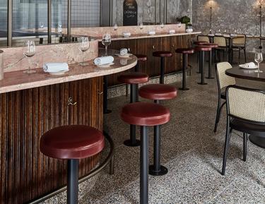 A modern restaurant interior with a contemporary design featuring plants, red ceiling, hanging lights, wooden bar counter, and seating area