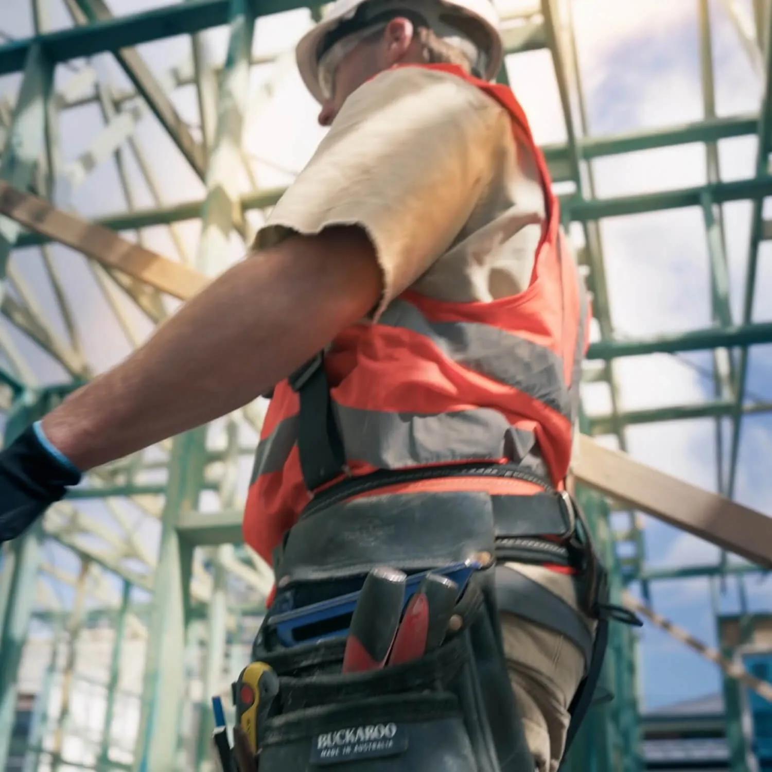 Worker in construction site gear standing by scaffolding, facing away from camera