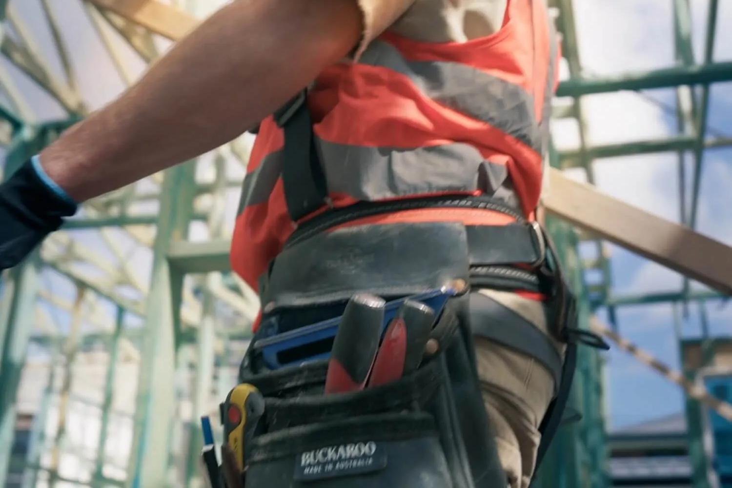 Worker in construction site gear standing by scaffolding, facing away from camera