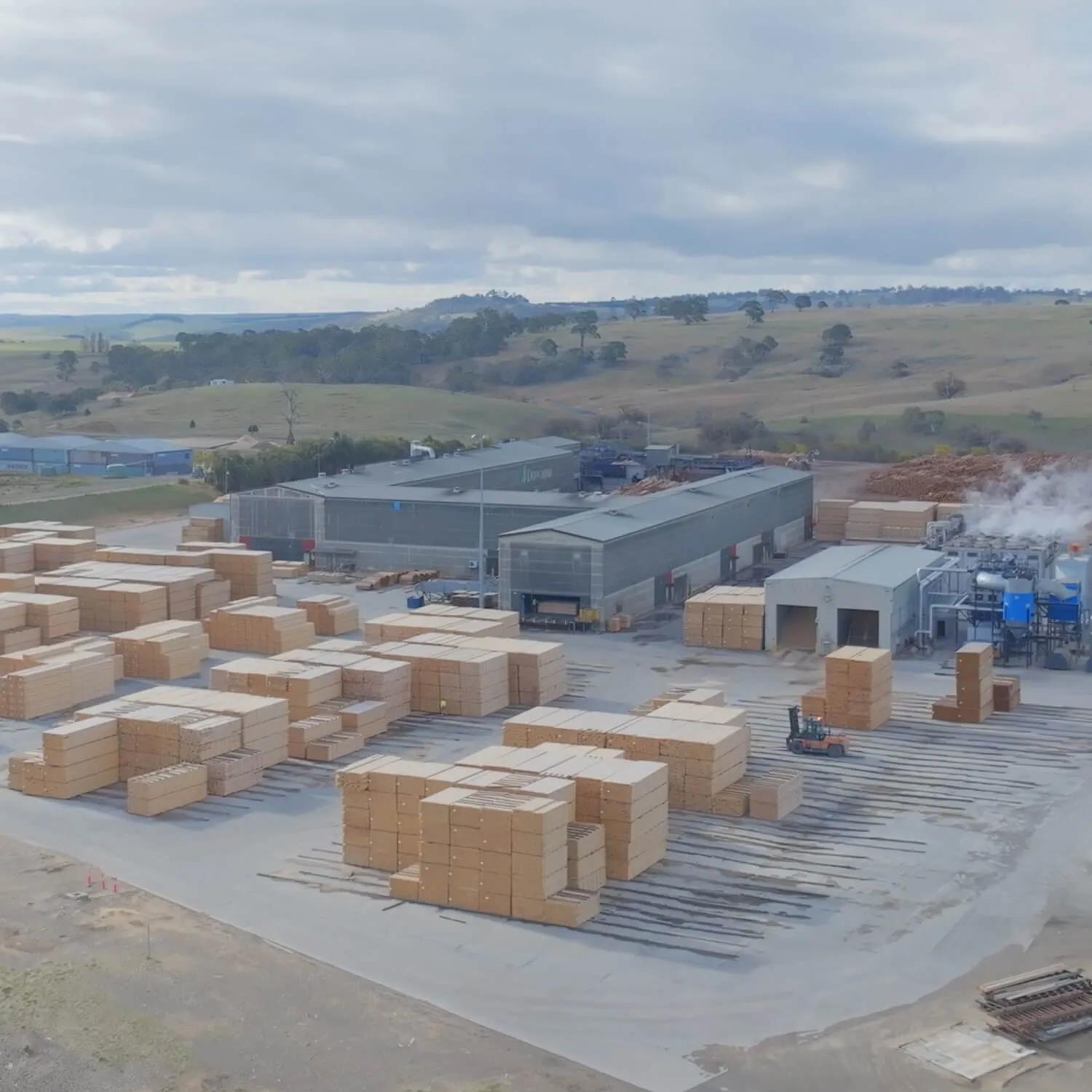Aerial view of a timber yard with numerous piles of wood and machinery in the background