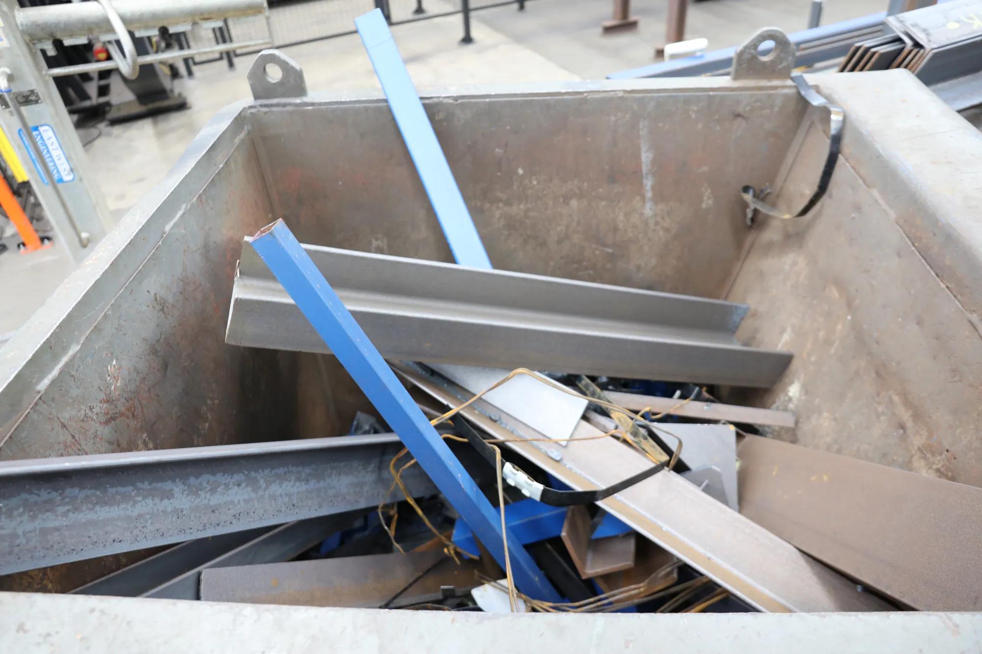 Mixed metal scrap and steel sections inside recycling bin.
